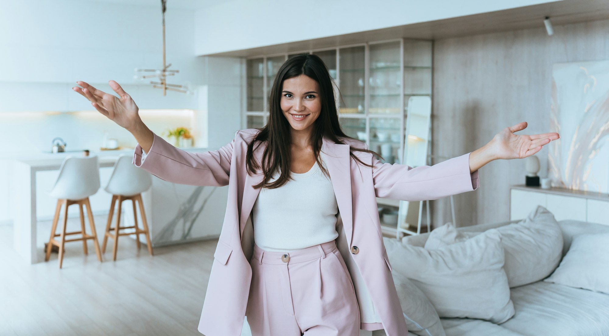 cheerful Asian realtor girl in a suit spreads arms and invited to inspect apartment in a new house